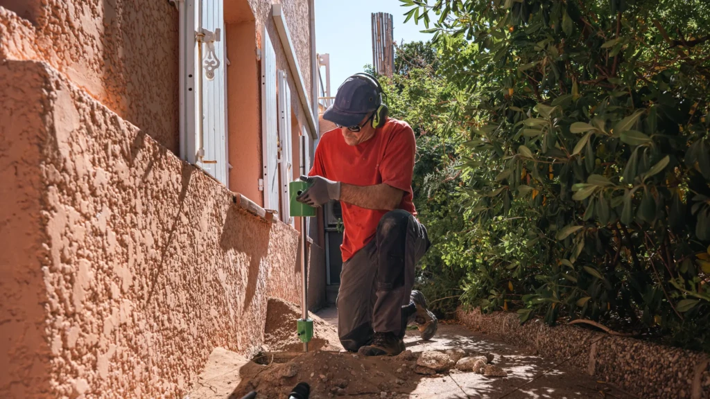 Diagnostic géotechnique G5 : technicien Beasol examinant le pied d’un mur de maison